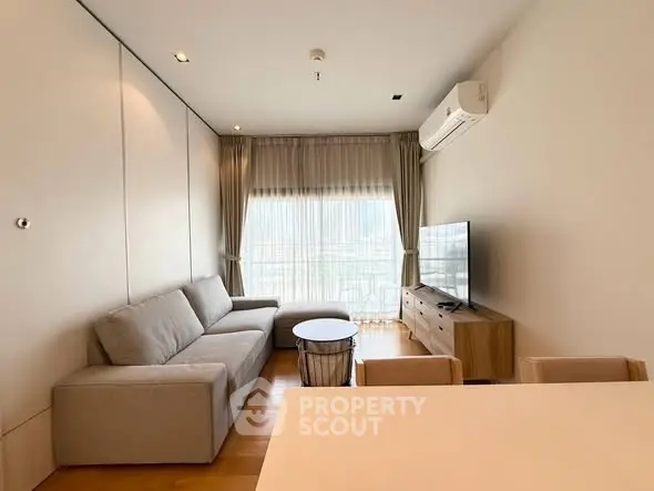 Modern living room with sleek furniture and large window offering natural light.