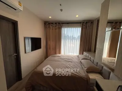 Cozy bedroom with modern decor, featuring a wall-mounted TV and large window with curtains.