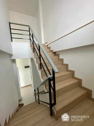 Modern staircase with sleek metal railings and wooden steps, leading to a bright, airy upper level in a contemporary home.