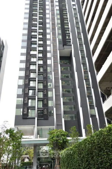 Modern high-rise building exterior with sleek design and lush greenery at the entrance.