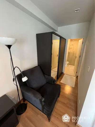 Cozy living space with sleek black sofa and hardwood floors leading to a bright, modern bathroom, perfect for urban living.