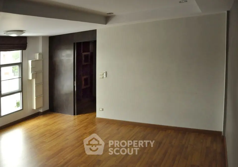 Spacious empty room with wooden flooring and large window, perfect for customization.