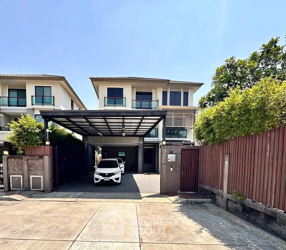 Modern two-story house with carport and lush greenery in a serene neighborhood.