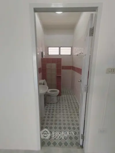 Compact bathroom with geometric tile flooring and red accent tiles, featuring a toilet and sink.
