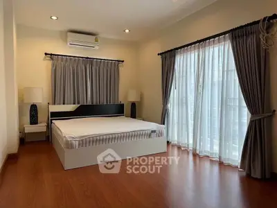 Spacious bedroom with large windows and elegant curtains, featuring a modern bed and wooden flooring.