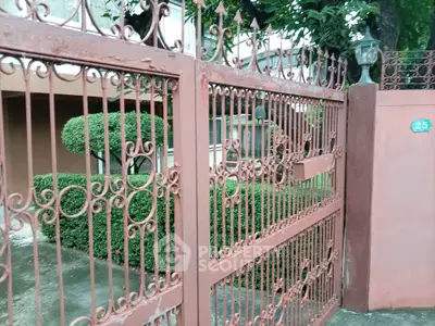 Elegant wrought iron gate with lush greenery in a residential setting.