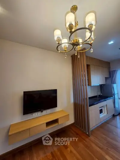Modern living room with elegant chandelier and compact kitchen in open layout apartment.