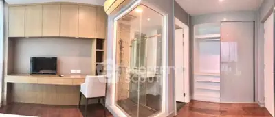 Modern bedroom with built-in desk, TV, and glass-enclosed shower in a stylish apartment.