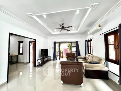 Spacious living room with modern furniture and ceiling fan, featuring large windows and elegant decor.