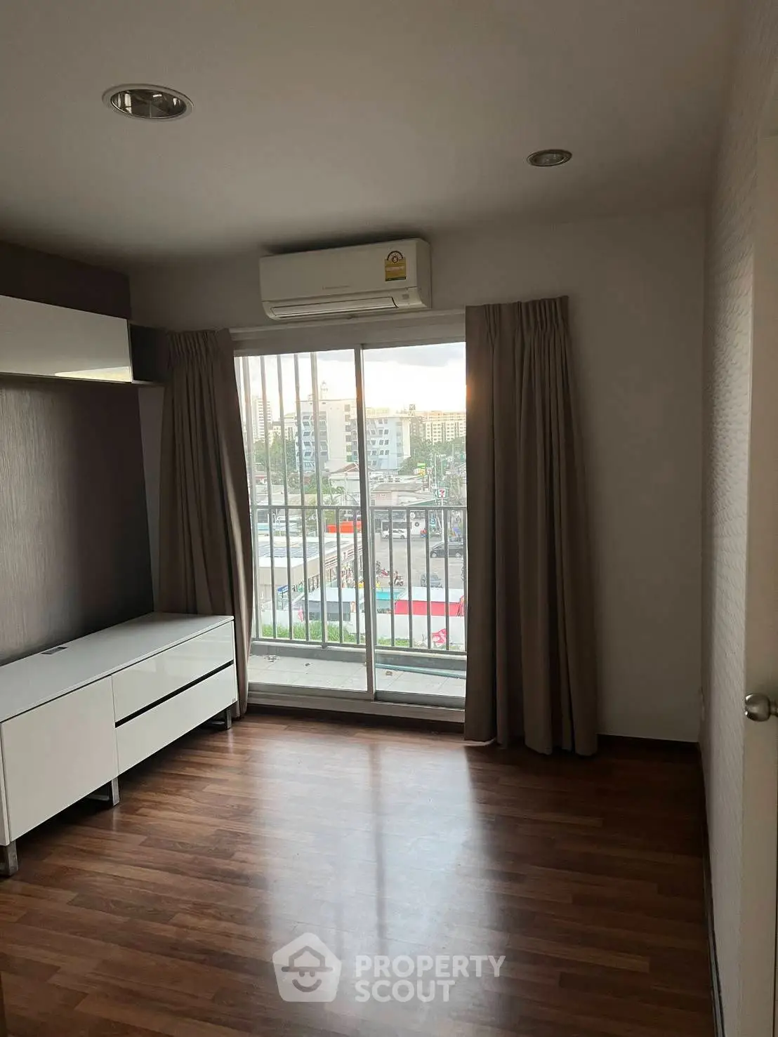 Spacious room with wooden flooring and large window offering city views