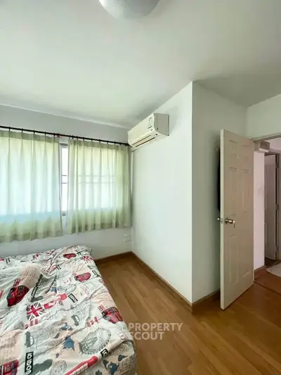 Cozy bedroom with wooden flooring, air conditioning, and natural light through large windows.