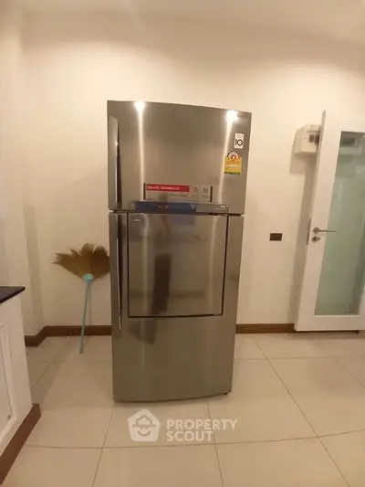 Modern kitchen with sleek stainless steel refrigerator and clean tile flooring.