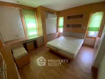 Spacious bedroom with wooden flooring and built-in furniture, featuring a large window for natural light.