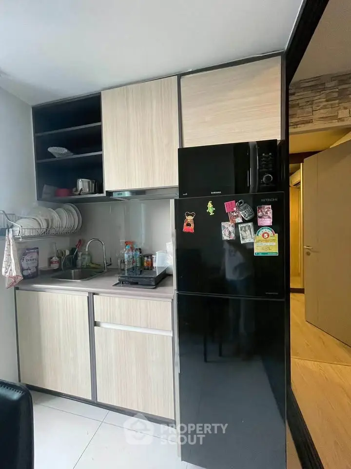 Modern compact kitchen with sleek black fridge and wooden cabinets, ideal for urban living.