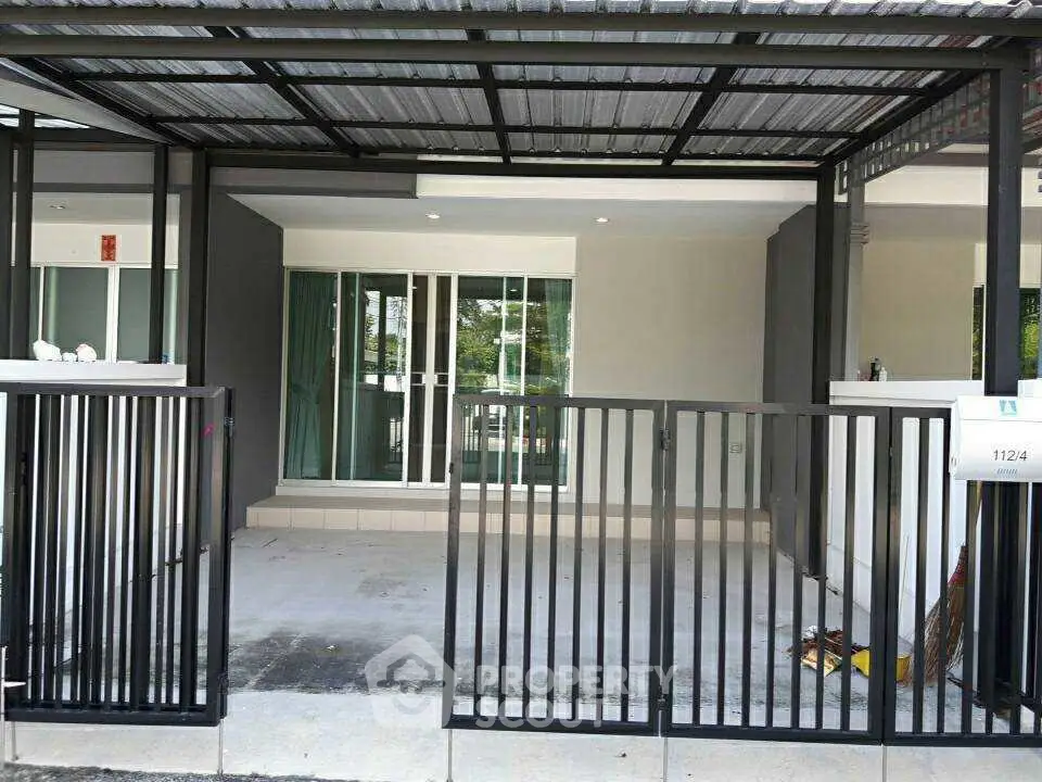 Modern townhouse entrance with sleek metal gate and covered parking area.