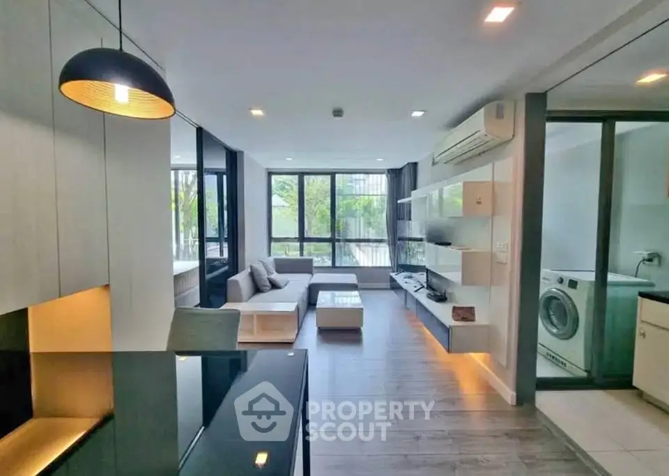 Modern living room with open layout and stylish decor, featuring large windows and a washing machine area.