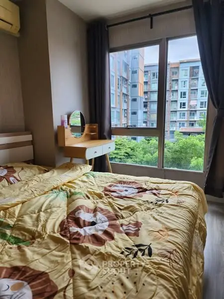 Cozy bedroom with large window offering a view of modern apartment buildings.