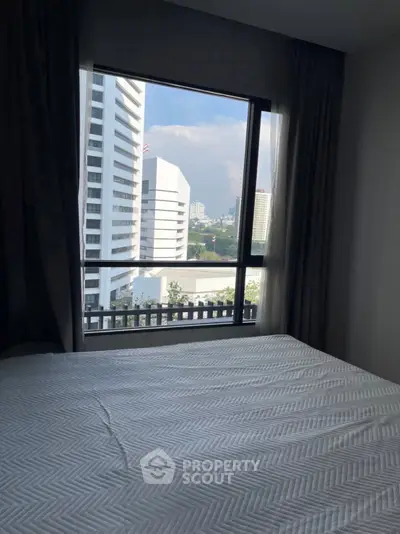 Spacious bedroom with city view through large window in modern apartment.