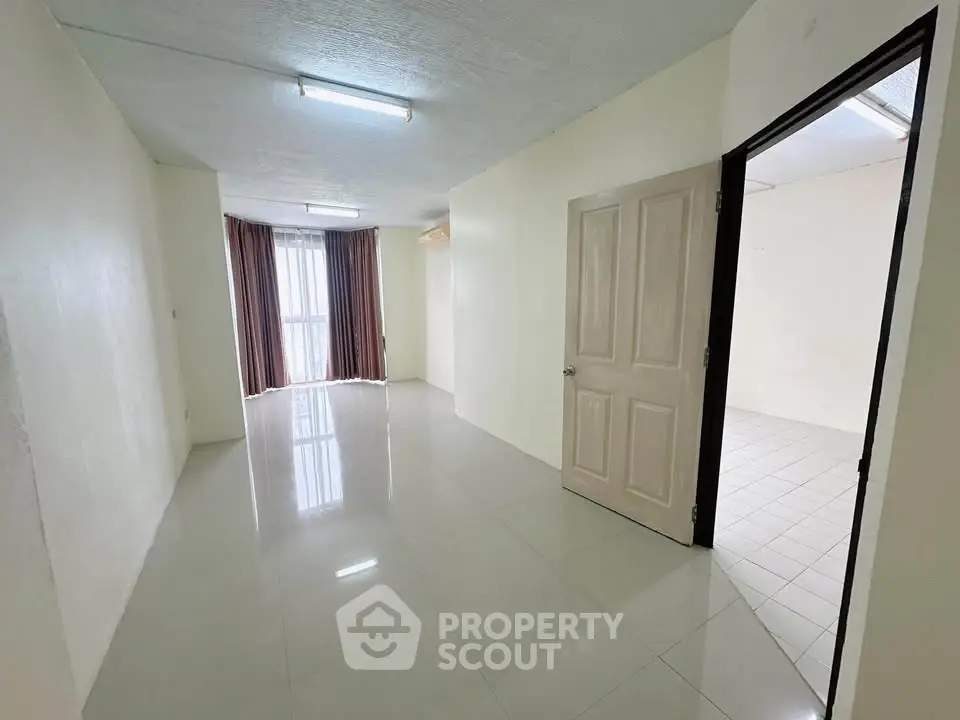 Spacious empty room with tiled floor and large window, ideal for customization.