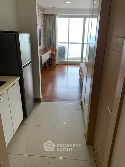 Modern apartment hallway leading to a bright living room with large windows and balcony view.