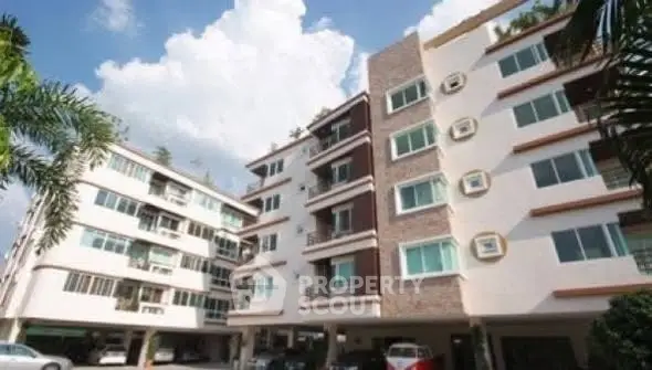 Modern apartment building exterior with multiple floors and parking area, showcasing urban living.