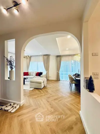 Elegant living room with modern decor and wooden flooring, featuring large windows and stylish lighting.