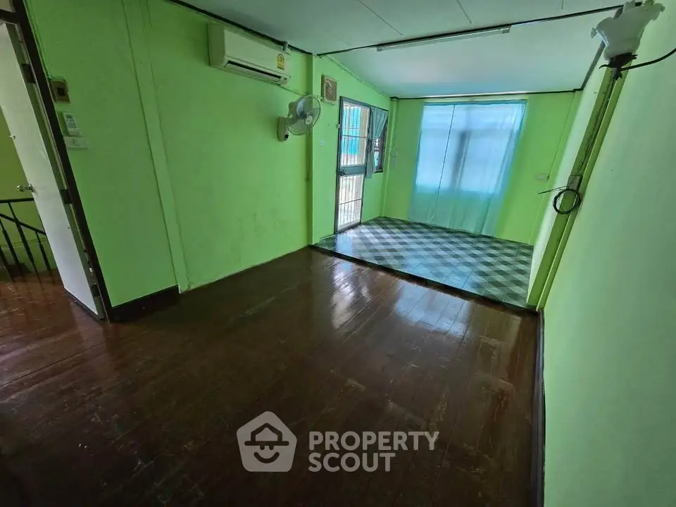 Spacious room with vibrant green walls and wooden flooring, featuring air conditioning and natural light.
