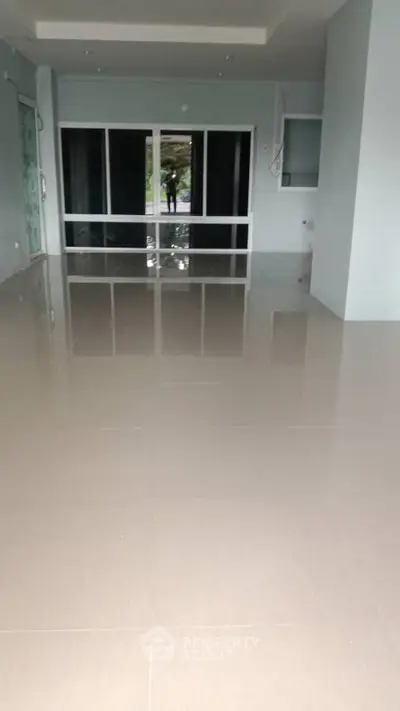 Spacious empty room with glossy tiled flooring and large glass doors leading outside.