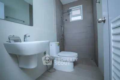 Modern bathroom with sleek fixtures and neutral tiles, featuring a shower and toilet.