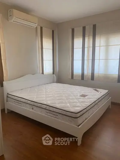 Spacious bedroom with large windows and air conditioning, featuring a comfortable bed and wooden flooring.