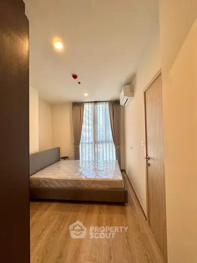 Modern bedroom with large window and wooden flooring in a stylish apartment.