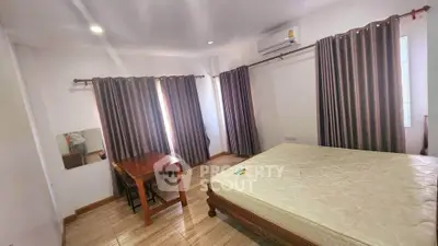 Spacious bedroom with large windows and elegant curtains, featuring a wooden bed and a cozy table setup.