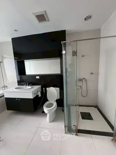 Modern bathroom with sleek black and white design, featuring a glass shower and stylish fixtures.