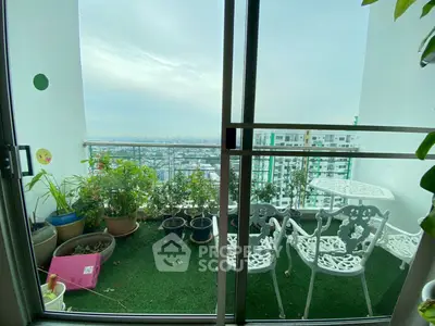 Charming balcony with city view, featuring white outdoor furniture and lush potted plants.