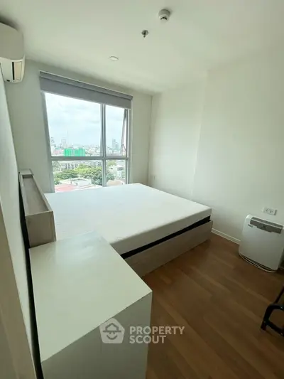 Bright bedroom with large window offering city view, featuring minimalist decor and wooden flooring.