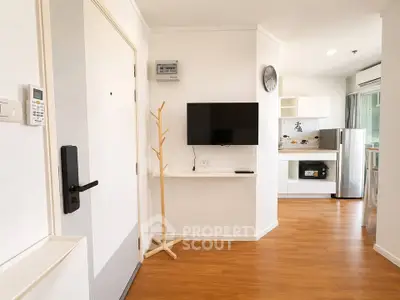 Modern apartment interior with open kitchen and wall-mounted TV, featuring wooden flooring and bright lighting.