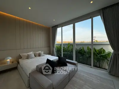 Luxurious bedroom with large windows and garden view, featuring modern decor and cozy seating area.