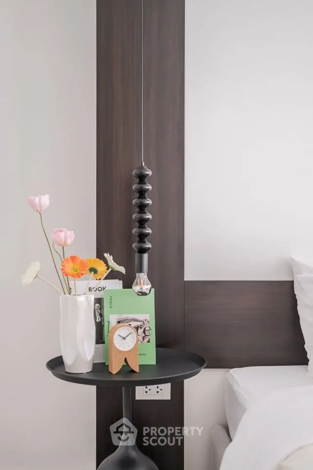 Modern bedroom with stylish decor and elegant lighting, featuring a bedside table with flowers and a clock.