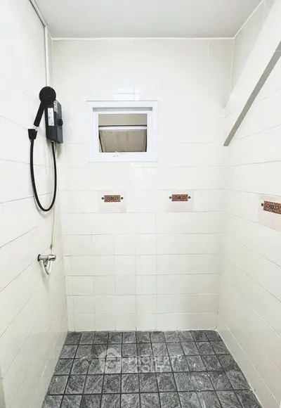 Modern bathroom with tiled walls and floor, featuring a shower area and small window for ventilation.