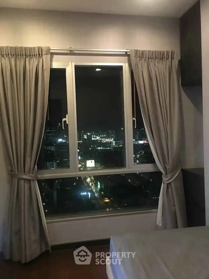 Cozy bedroom with stunning city night view from large window, perfect for urban living.