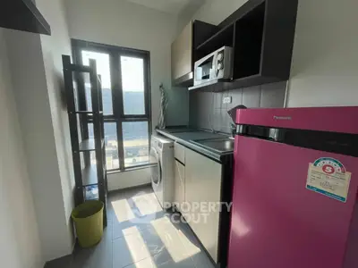 Modern kitchen with pink fridge, washing machine, and ample natural light.