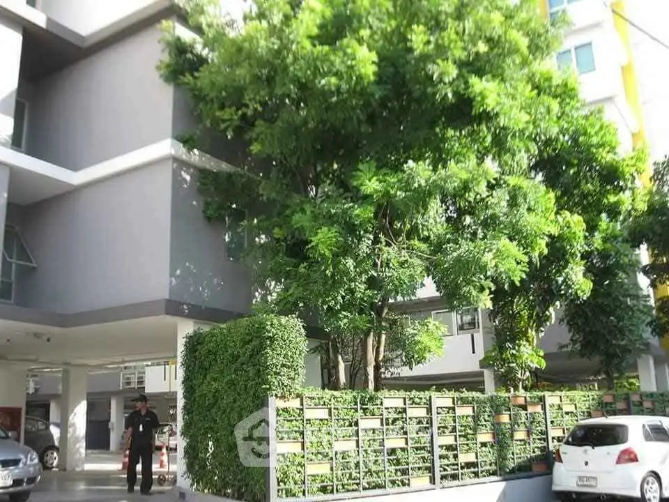 Modern apartment building exterior with lush greenery and parking area.