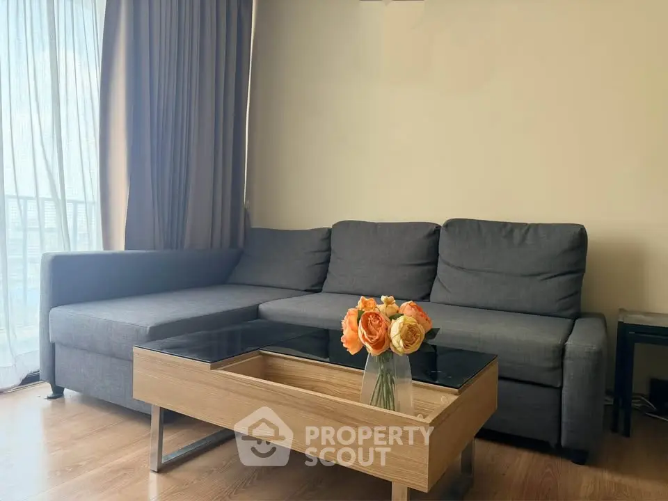 Modern living room with sleek gray sofa and elegant glass-top coffee table, accented by vibrant floral arrangement.