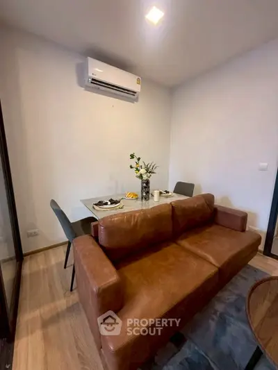 Cozy living room with brown leather sofa and dining table, featuring modern air conditioning.