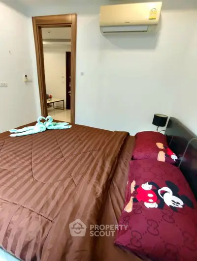 Cozy bedroom with brown bedding and playful Mickey Mouse pillows, featuring a wall-mounted air conditioner.