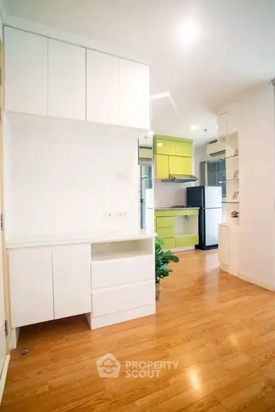 Modern kitchen with sleek white cabinets and vibrant green accents, featuring wooden flooring and ample natural light.
