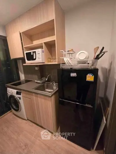 Modern compact kitchen with wooden cabinets, black fridge, microwave, and washing machine.