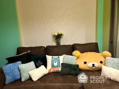 Cozy living room corner featuring a plush brown sofa adorned with an array of colorful cushions and a charming teddy bear pillow.