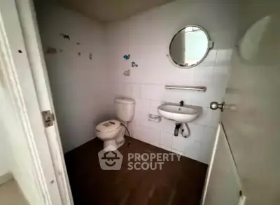 Compact bathroom with white tiles, round mirror, and standard fixtures.
