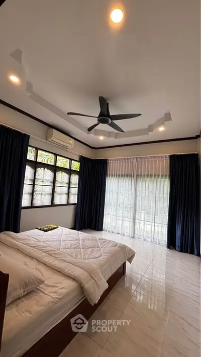 Spacious bedroom with large windows and ceiling fan, offering natural light and comfort.